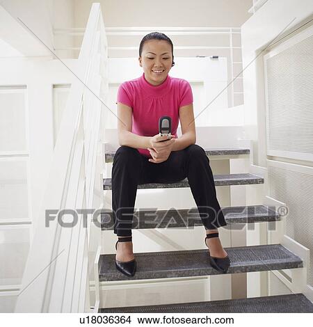 Low angle view of a businesswoman sitting on a staircase and holding a mobile phone View Large Photo Image Picture - Low angle view of a businesswoman sitting on a staircase and holding a mobile phone. Fotosearch