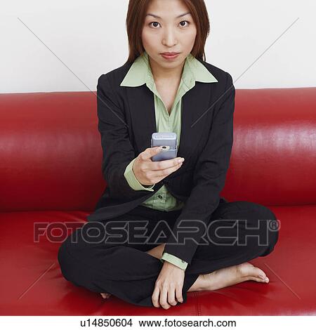 Picture - Portrait of a businesswoman sitting on a couch and holding a mobile phone. Fotosearch