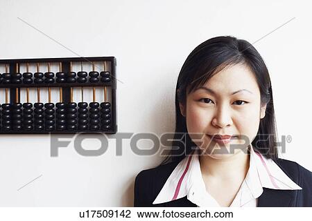 Stock Image - Portrait of a businesswoman smiling near an abacus on a wall. Fotosearch