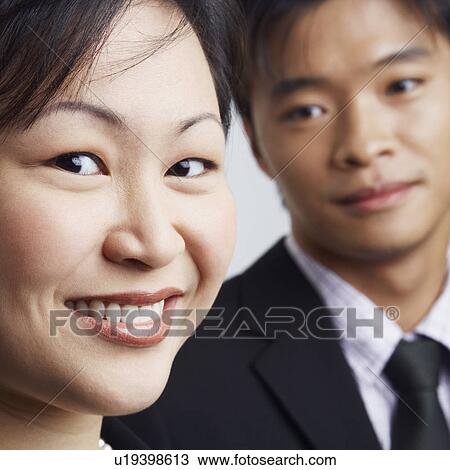 Stock Image - Portrait of a businesswoman smiling with a businessman beside her. Fotosearch