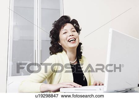 Stock Photo - Portrait of a businesswoman using a laptop laughing. Fotosearch