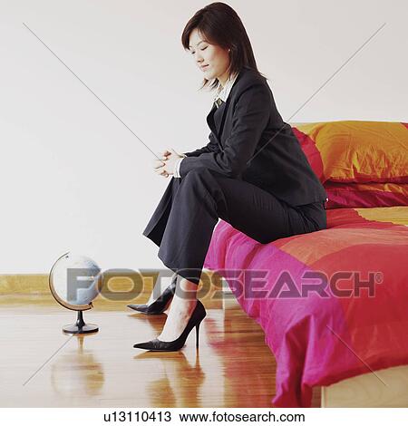 Stock Image - Side profile of a businesswoman sitting on the bed and looking at a globe. Fotosearch
