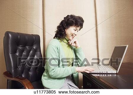 Stock Photography - Side profile of a businesswoman using a laptop smiling. Fotosearch