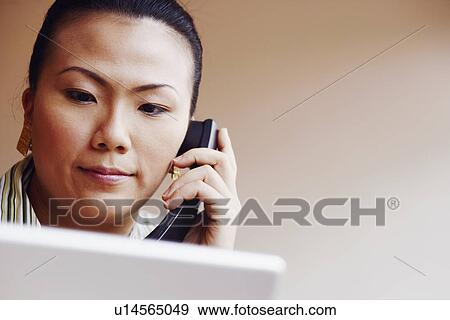 Stock Photo - Close-up of a young woman talking on the telephone and looking at a laptop. Fotosearch