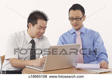 Stock Photo - Close-up of two businessmen sitting in front of a laptop. Fotosearch