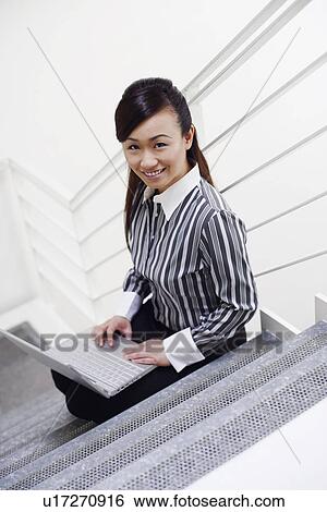 High angle view of a young woman sitting on a staircase and using a laptop View Large Photo Image Stock Photograph - High angle view of a young woman sitting on a staircase and using a laptop. Fotosearch
