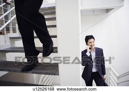 Stock Photo - Low section view of a man walking down stairs with another businessman talking on a mobile phone. Fotosearch