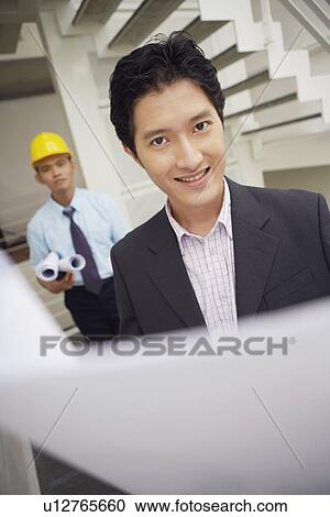 Stock Image - Portrait of a businessman holding blueprints and smiling. Fotosearch