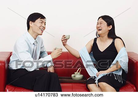 Stock Image - Close-up of a businessman and a mid adult man sitting together and holding tea cups. Fotosearch