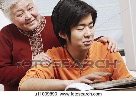 Close-up of a grandson using a computer with his grandmother standing behind him View Large Photo Image Stock Image - Close-up of a grandson using a computer with his grandmother standing behind him. Fotosearch