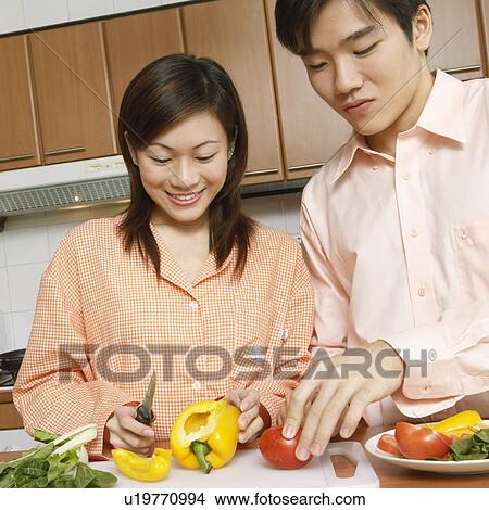 Picture - Close-up of a young couple cutting vegetables at a kitchen counter. Fotosearch