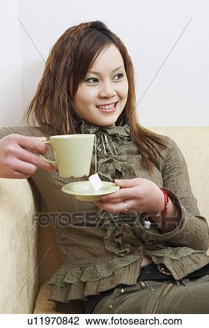 Stock Image - Close-up of a young woman holding a cup of tea smiling. Fotosearch