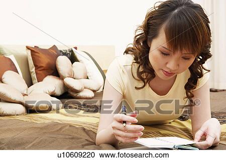 Stock Image - Close-up of a young woman lying on the bed and looking at a diary. Fotosearch