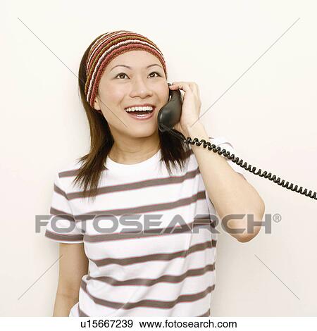 Close-up of a young woman talking on the telephone and looking cheerful View Large Photo Image Stock Photo - Close-up of a young woman talking on the telephone and looking cheerful. Fotosearch