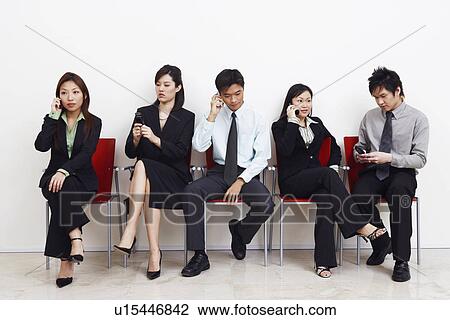 Stock Image - Two businessmen and three businesswomen sitting with mobile phones. Fotosearch