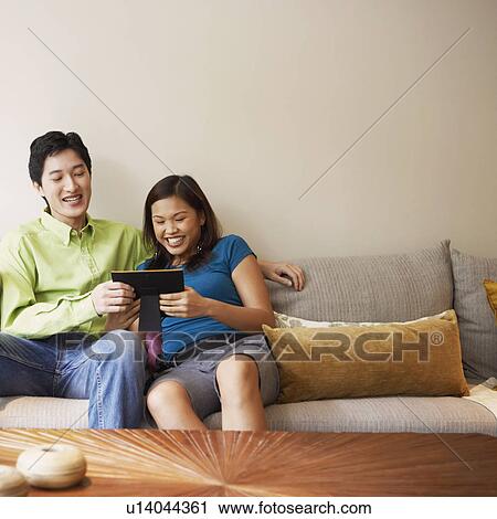 Stock Image - Young couple looking at a picture frame and smiling on a couch. Fotosearch