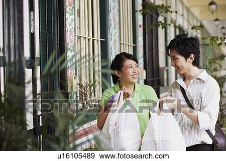Stock Photo - Young couple looking at each other and holding plastic bags. Fotosearch