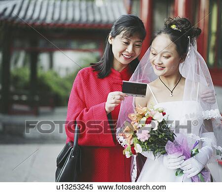 Young woman in the wedding dress looking at a photograph with another woman View Large Photo Image Stock Photography - Young woman in the wedding dress looking at a photograph with another woman. Fotosearch