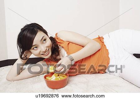 Young woman lying on her side holding a slice of orange View Large Photo Image Stock Photograph - Young woman lying on her side holding a slice of orange. Fotosearch
