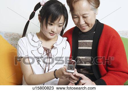 Young woman sitting together with her grandmother holding a mobile phone View Large Photo Image Stock Image - Young woman sitting together with her grandmother holding a mobile phone. Fotosearch