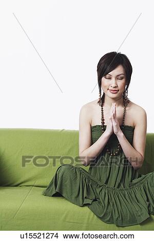 Close-up of a young woman sitting on a couch in a prayer position View Large Photo Image Picture - Close-up of a young woman sitting on a couch in a prayer position. Fotosearch