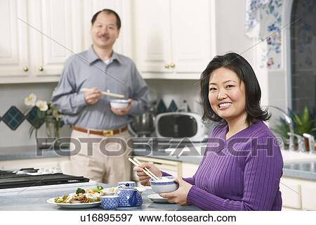 Portrait of a mature woman holding a pair of chopsticks with a senior man standing behind her View Large Photo Image Stock Photo - Portrait of a mature woman holding a pair of chopsticks with a senior man standing behind her. Fotosearch