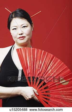 Stock Photo - Portrait of a mid adult woman holding a folding fan. Fotosearch