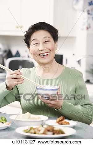 Stock Photo - Portrait of a senior woman holding a pair of chopsticks and a bowl. Fotosearch