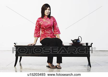 Stock Image - Portrait of a young woman sitting on a table. Fotosearch
