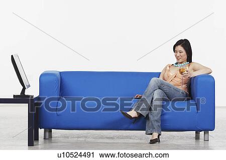 Stock Image - Young woman holding a glass of red wine sitting on a couch. Fotosearch