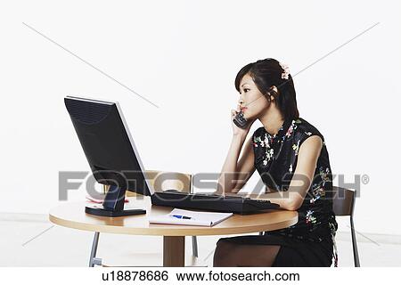 Young woman sitting in front of a computer talking on the telephone View Large Photo Image Stock Photograph - Young woman sitting in front of a computer talking on the telephone. Fotosearch