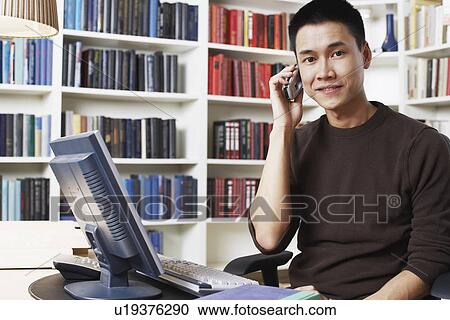 Close-up of a businessman sitting in front of a computer and using a mobile phone View Large Photo Image Stock Image - Close-up of a businessman sitting in front of a computer and using a mobile phone. Fotosearch