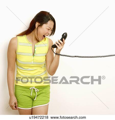 Stock Photo - Close-up of a young woman holding a telephone receiver and laughing. Fotosearch