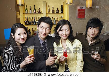 Stock Image - Four friends standing in front of a bar counter holding drinks in glasses. Fotosearch