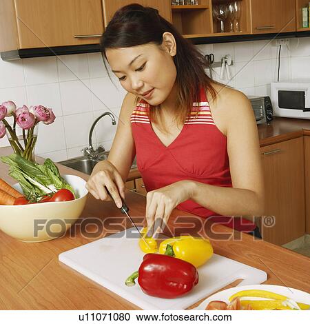 Stock Image - High angle view of a young woman cutting vegetables at the kitchen. Fotosearch