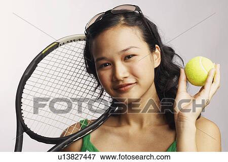 Stock Photo - Portrait of a young woman holding a tennis ball and a tennis racket. Fotosearch
