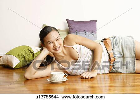 Portrait of a young woman lying on the floor with a tea cup in front of her View Large Photo Image Picture - Portrait of a young woman lying on the floor with a tea cup in front of her. Fotosearch