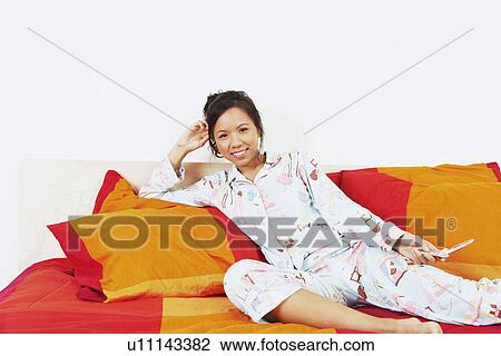 Stock Image - Portrait of a young woman reclining on the bed and smiling. Fotosearch