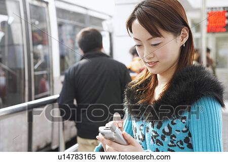 Stock Photography - Side profile of a young woman operating a mobile phone with a digitized pen. Fotosearch