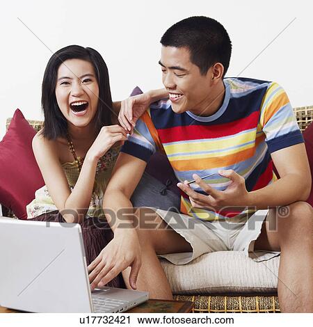 Stock Image - Young woman sitting beside a young man holding a credit card and using a laptop. Fotosearch