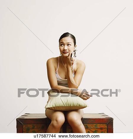 Picture - Young woman sitting on a trunk and listening to music. Fotosearch