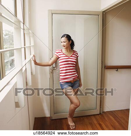 Picture - Young woman standing at a doorway and smiling. Fotosearch