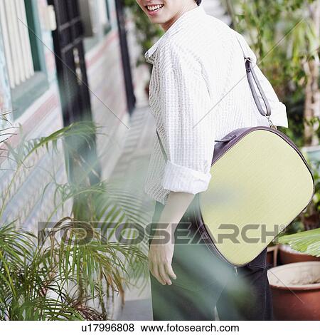 Stock Photo - Portrait of a young man carrying a bag and smiling. Fotosearch