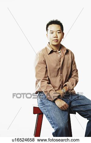 Portrait of a young man sitting on a stool View Large Photo Image Stock Photo - Portrait of a young man sitting on a stool. Fotosearch