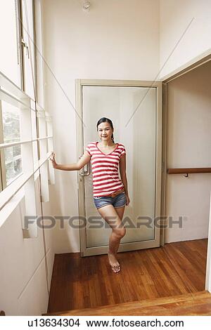 Picture - Portrait of a young woman standing at a door and smiling. Fotosearch