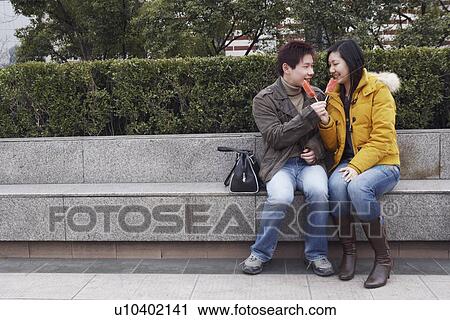 Young man and a young woman sitting on a ledge eating watermelon View Large Photo Image Stock Image - Young man and a young woman sitting on a ledge eating watermelon. Fotosearch