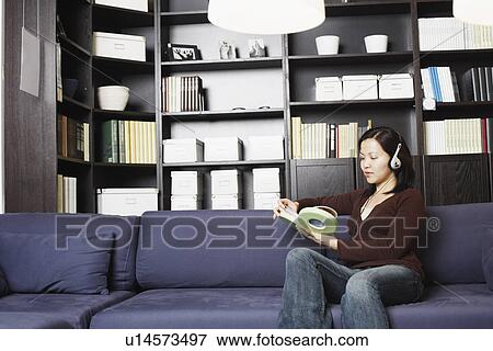 Stock Photo - Young woman holding a CD case listening to music on headphones. Fotosearch