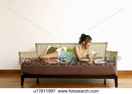 Stock Photo - Young woman using a laptop on a couch and smiling. Fotosearch