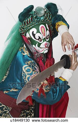 Stock Image - Side profile of a male Chinese opera performer holding a weapon. Fotosearch