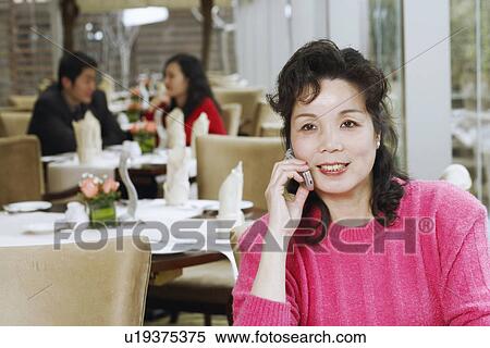 Stock Photography - Mature woman sitting in a restaurant using a mobile phone. Fotosearch